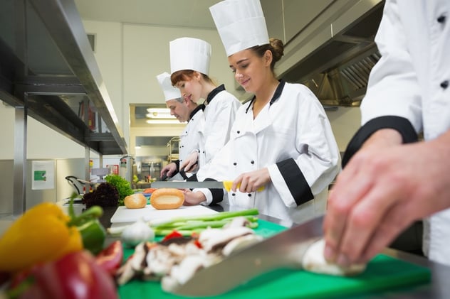 Four chefs preparing food at counter in a row in a professional kitchen.jpeg